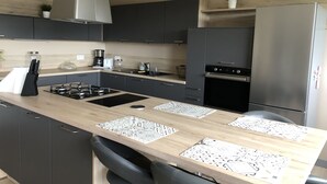 Une cuisine moderne avec des meubles de couleur sombre, un réfrigérateur en acier inoxydable, une cuisinière à gaz et un plan de travail en bois agrémenté de sets de table.