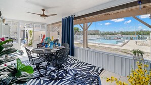 An outdoor patio with a table and chairs, a ceiling fan, and a view of a swimming pool.