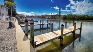 A wooden dock extending into calm water, surrounded by a white fence and a building with a balcony.