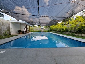 A swimming pool with a shaded area overhead, surrounded by greenery and a small seating area with a swing set. - CMJ Private Resort  (Indang)