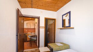 Una habitación pequeña y acogedora con techo de madera, una cama con colcha verde a rayas, una mesita y un espejo en la pared.