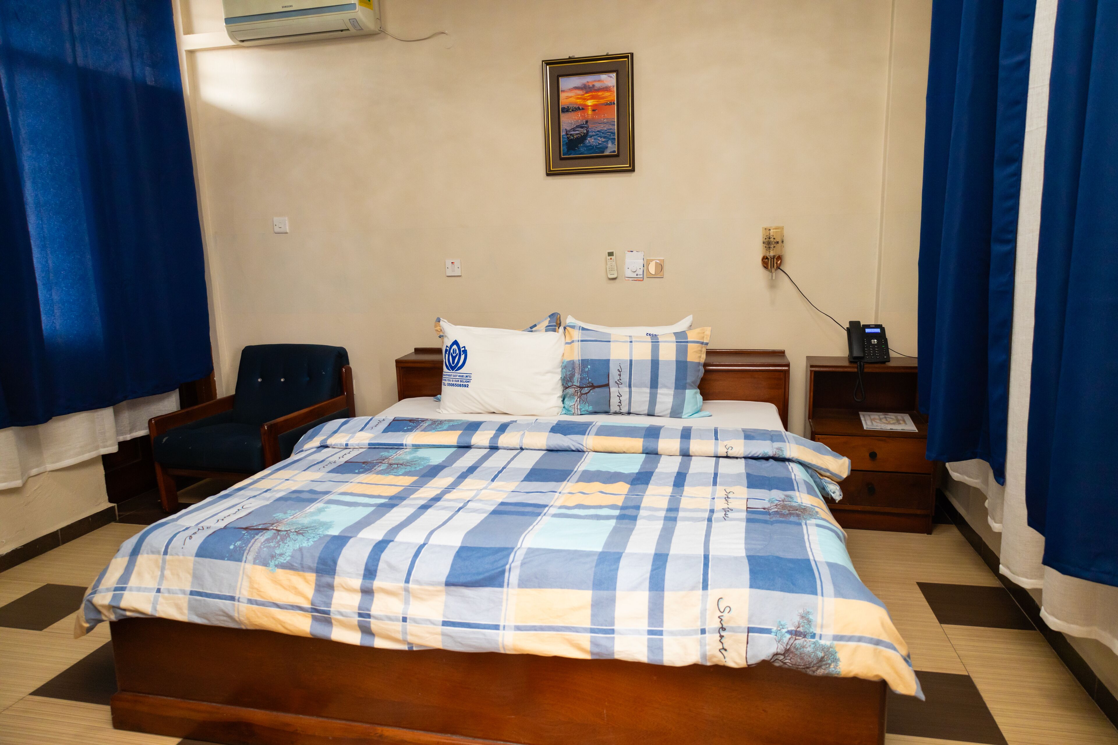 A neatly made bed with a checkered bedspread, a bedside table with a lamp, and a chair.
