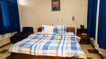 A neatly made bed with a checkered bedspread, a bedside table with a lamp, and a chair.