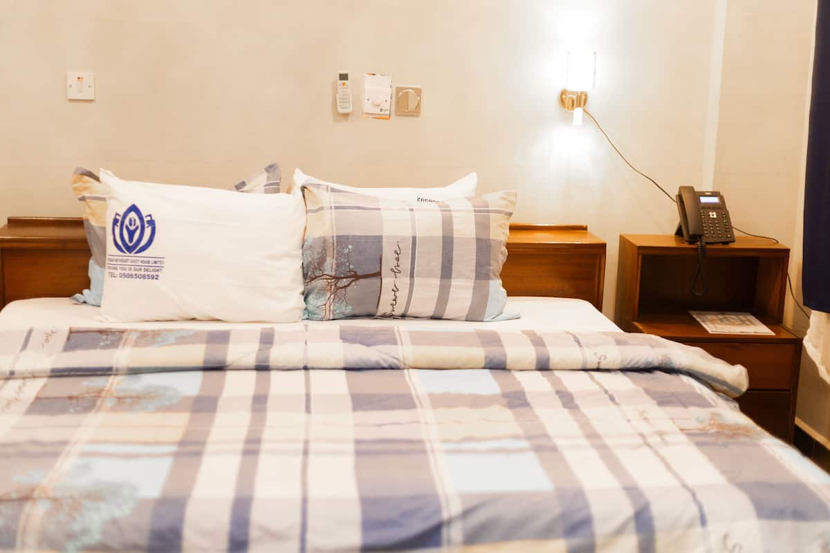 Habitación de hotel con cama, almohadas, mesita de noche con teléfono y enchufe de pared.