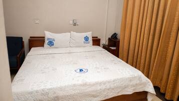 Habitación de hotel con cama, dos almohadas, mesita de noche, teléfono y cortina.