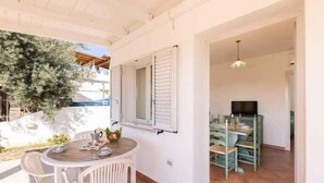 Una habitación con una mesa y sillas de madera, un televisor y un balcón con vistas a árboles.