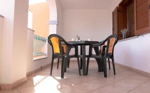 A small dining area with a round table and four chairs, a window with wooden shutters, and a tiled floor.