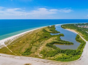 An aerial view of a coastal area with a beach, a waterway, and a small settlement.