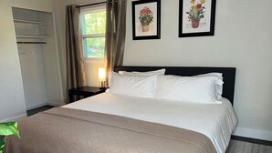 A neatly made bed with white linens, a bedside table with a lamp, and a framed botanical print on the wall.