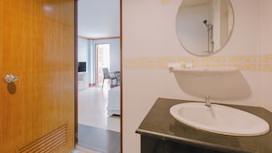 A bathroom with a wooden door, a sink with a mirror, and a tiled floor. - sunstar palace patong (Patong)