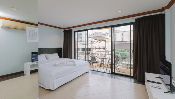 A hotel room with a bed, a desk with a TV, a balcony with chairs, and a view of buildings. - sunstar palace patong (Patong)