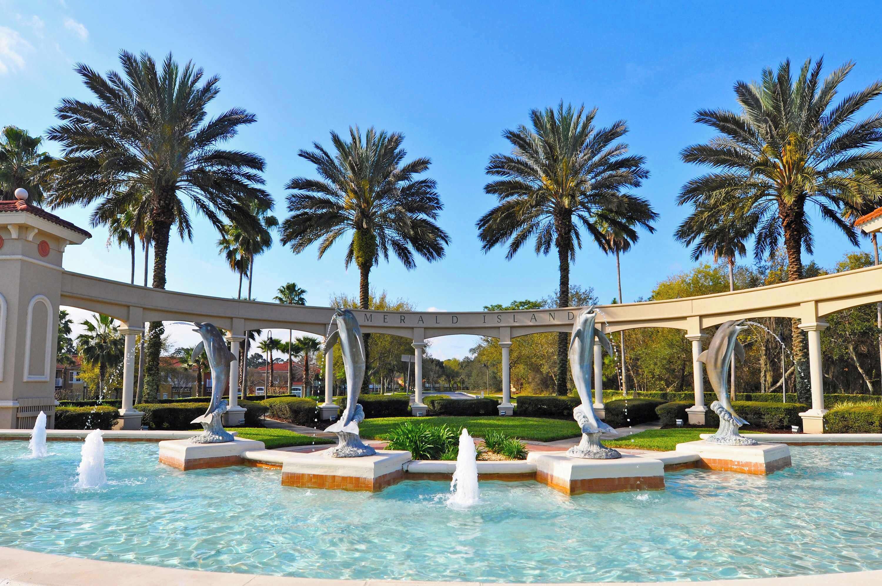 A pool area with dolphin sculptures, palm trees, and a sign reading 'MERALD ISLAND'.