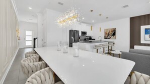 A modern kitchen with a white island, stainless steel appliances, and a chandelier.