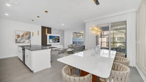 A modern kitchen with white cabinetry, a central island, and a dining area with a white table and beige upholstered chairs.