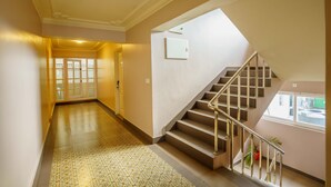 A spacious hallway with a patterned floor, a staircase with a handrail, and a door leading to another room.