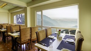A restaurant with high tables and chairs, a view of mountains, and a sign with 'NA' on the wall.