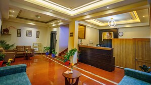 A hotel lobby with a reception desk, seating area, and potted plants.