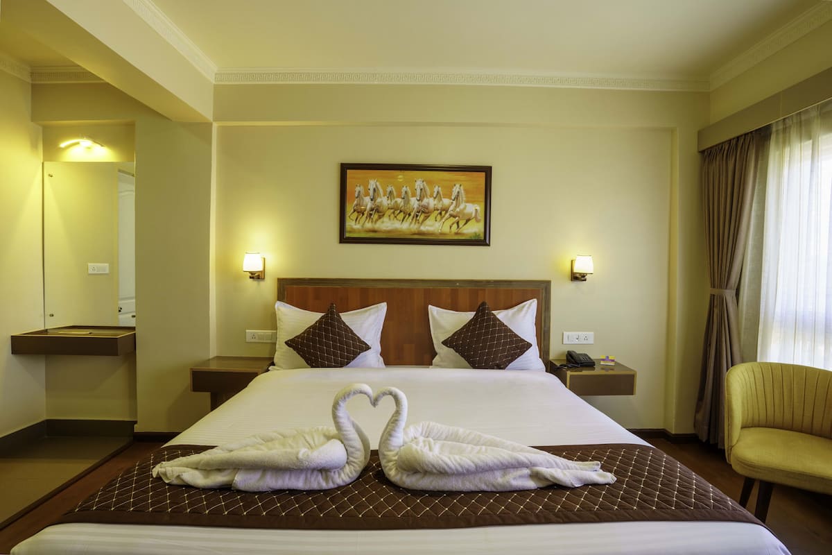 A hotel room with a large bed, two nightstands, a painting on the wall, and a chair by the window.