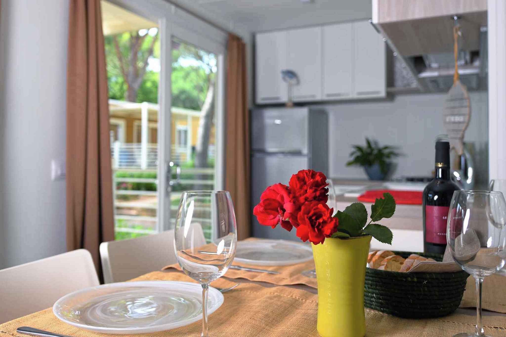 A dining table set with plates, wine glasses, and a vase with red flowers.