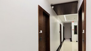 A hotel hallway with wooden doors, white walls, and a tiled floor. - Hotel Rajdev INN  (Ujjain)