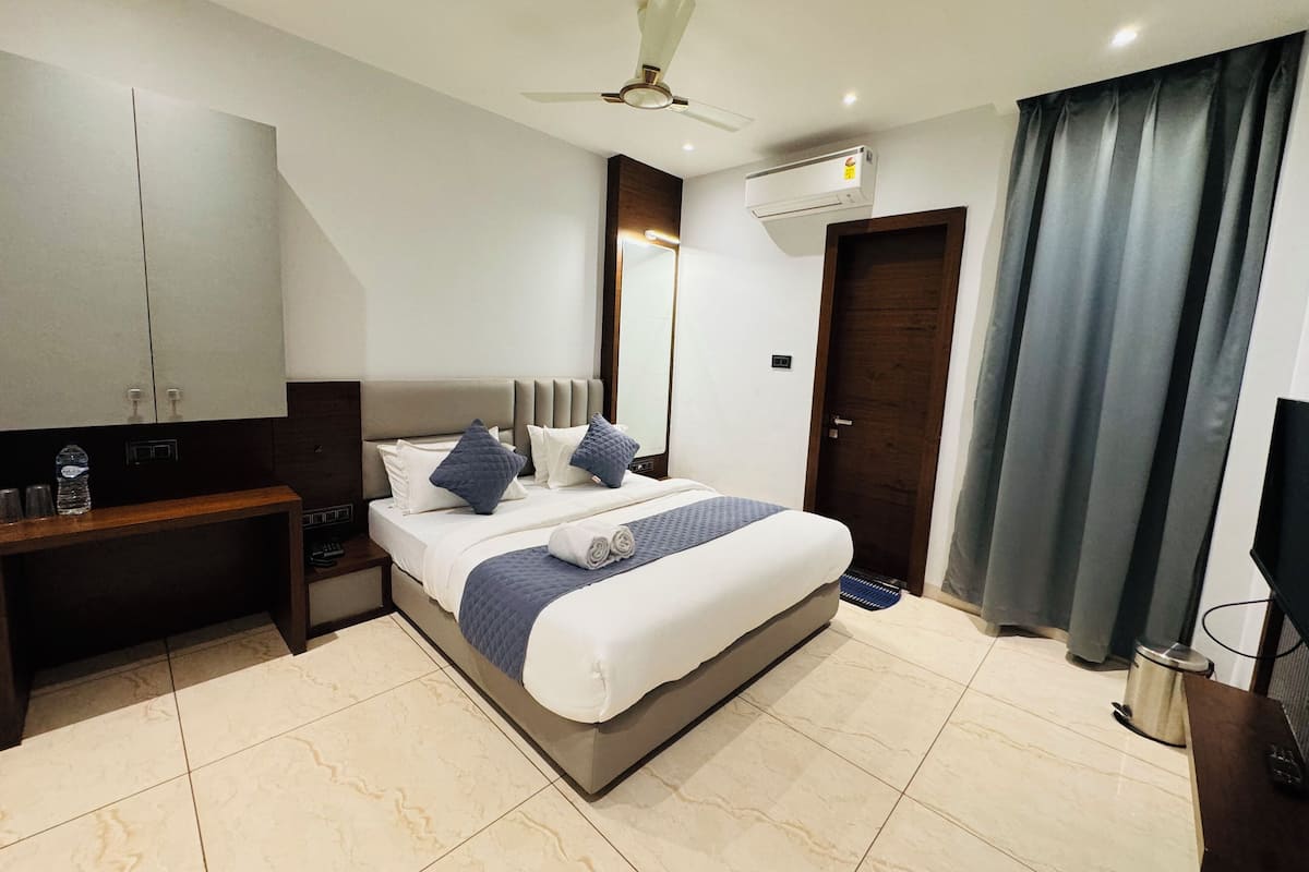 A modern hotel room with a bed, a desk, a wardrobe, an air conditioning unit, and a ceiling fan.