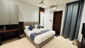A modern hotel room with a bed, a desk, a wardrobe, an air conditioning unit, and a ceiling fan.