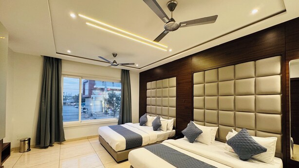 A hotel room with two beds, a large window, a ceiling fan, and a modern design. - Hotel Rajdev INN  (Ujjain)