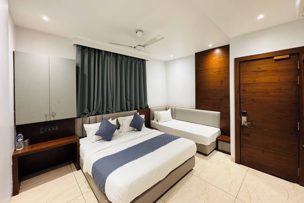 A modern hotel room with a large bed, a smaller bed, a wardrobe, a vanity, a mirror, a ceiling fan, and a door.