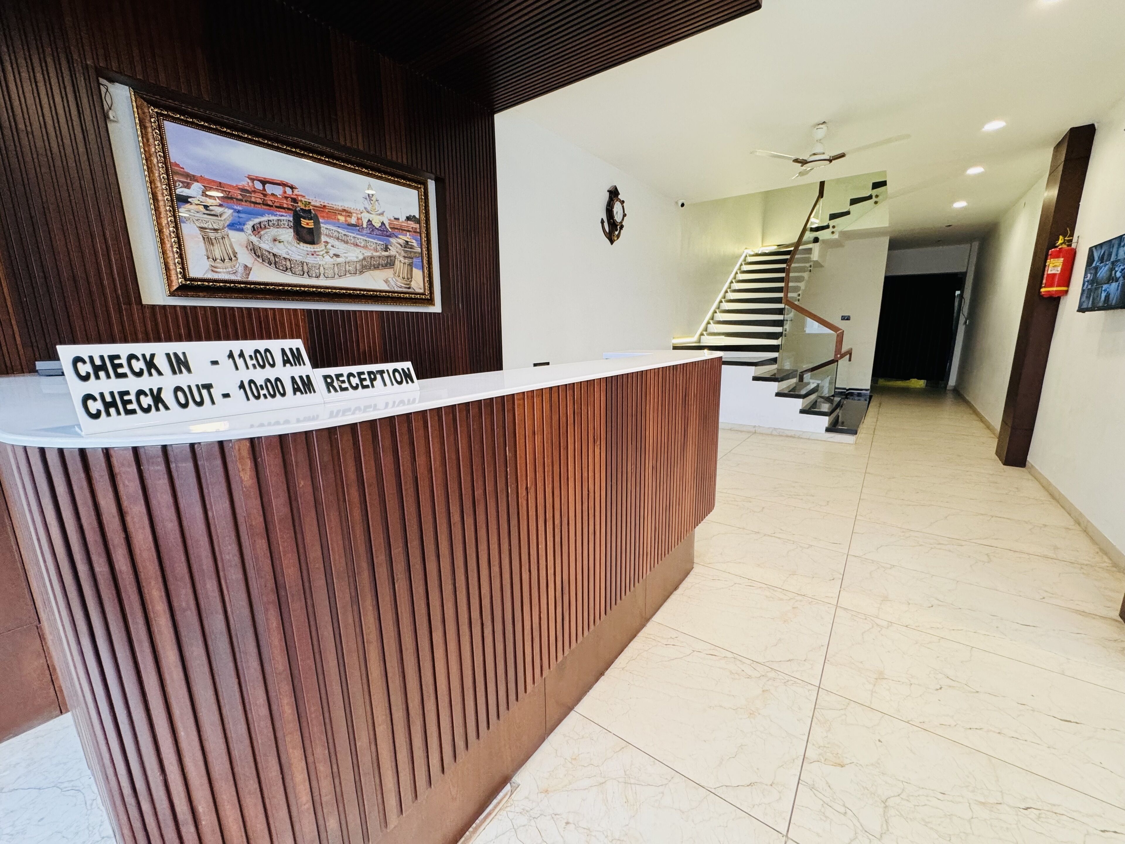 Bancada de recepção com sinalização de horários de check-in e check-out, escada ao fundo e câmera de segurança na parede.