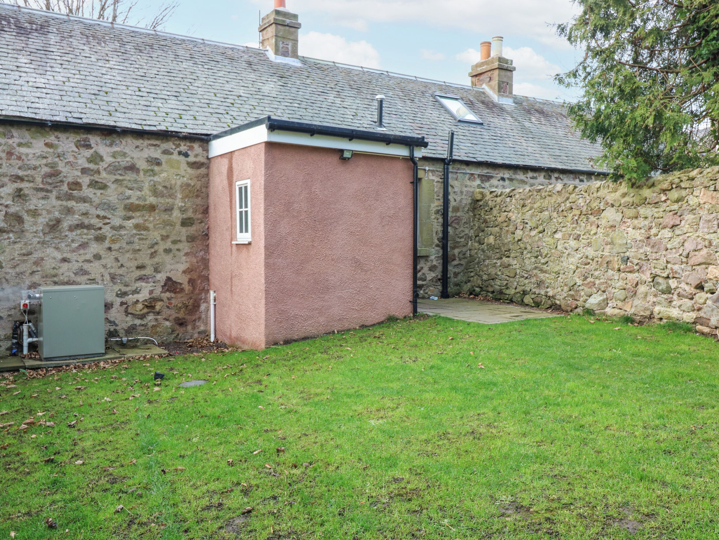 A stone building with a small brick extension, a grassy yard, and a utility box.
