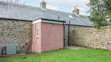 A stone building with a small brick extension, a grassy yard, and a utility box.