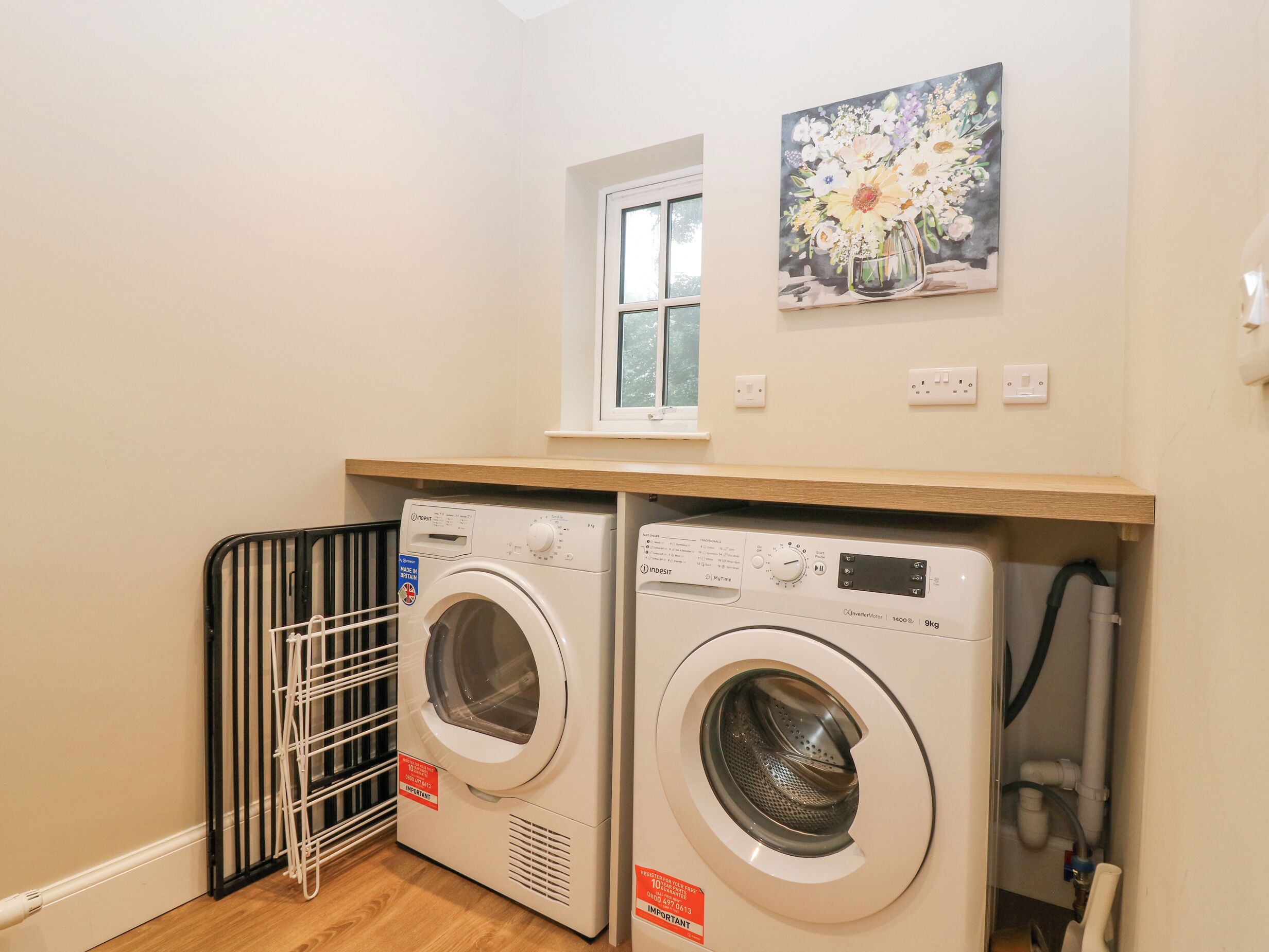 A laundry area with two washing machines, a drying rack, and a window with a painting above.