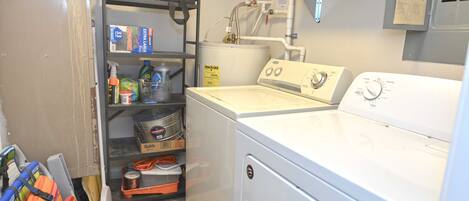 A laundry area with a washing machine, shelves with cleaning supplies, and a utility room with electrical panels.