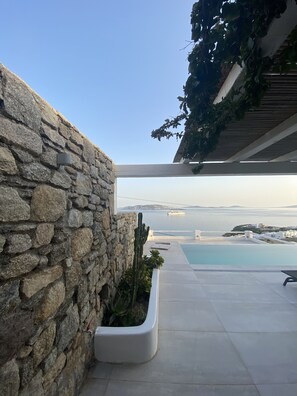 A stone wall with a planter, a pool, and a view of the sea and distant islands. - Mykonian Luxury Villa Azure w View Pool (Mykonos)