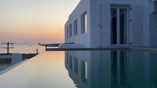 A modern white building with a reflective pool in front, a door, and windows. - Mykonian Luxury Villa Azure w View Pool (Mykonos)