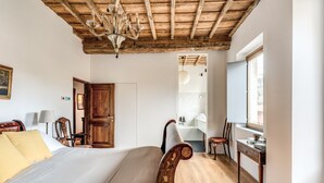 A bedroom with a wooden ceiling, a large bed, a wooden chair, a small table, and a window. - Trastevere Outstanding  4 BR Terraced Apartment (Roma)