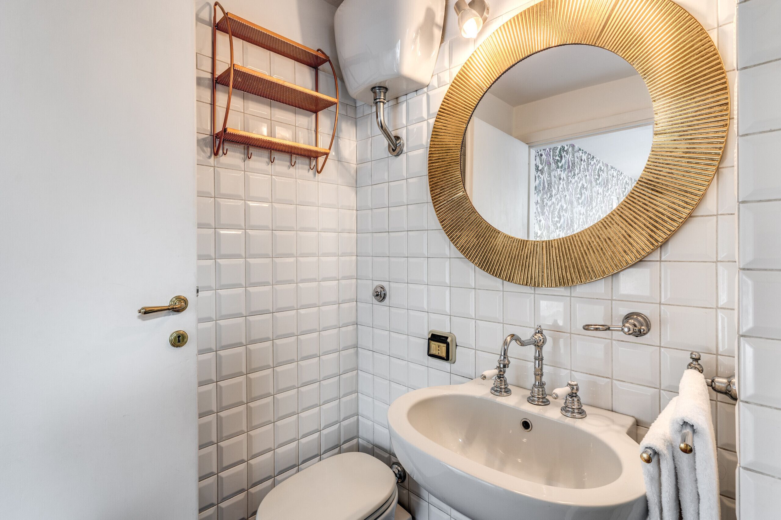 A bathroom with white tiled walls, a white sink, a gold-framed mirror, and a toilet.