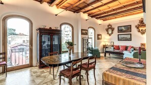 A spacious room with a wooden dining table, chairs, and a sofa. There are arched windows and a balcony visible. - Trastevere Outstanding  4 BR Terraced Apartment (Roma)