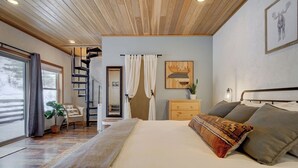 Une chambre avec un grand lit, un plafond en bois, un escalier et une vue sur l’extérieur.