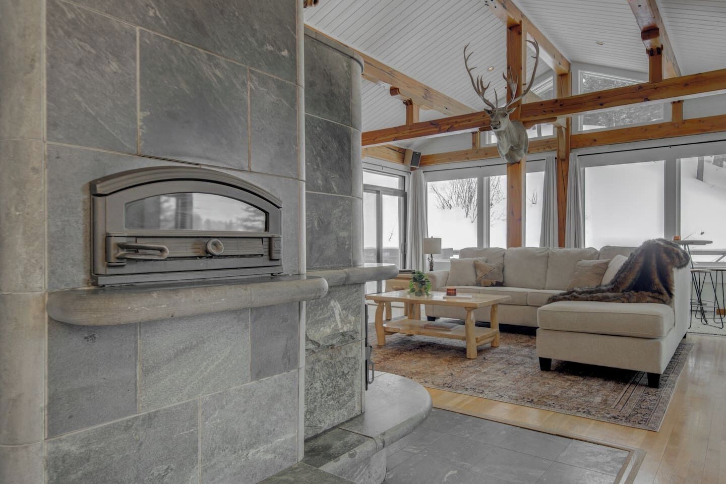 A modern living room with a stone fireplace, a sectional sofa, and a deer head mounted on the ceiling.