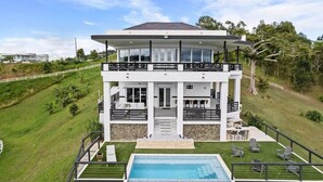Una casa moderna de dos pisos con un balcón grande, una piscina y un césped bien cuidado.