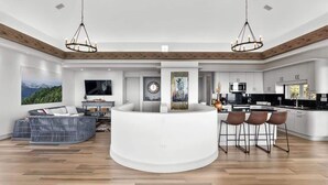 Una sala-comedor moderna de concepto abierto con una isla central, vigas de madera en el techo y un televisor grande.