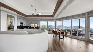 Cocina moderna con una isla curva, amplios ventanales con vistas a la montaña y un comedor con mesa y sillas.