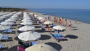 A beach with rows of white umbrellas and beach chairs, people sunbathing, and the sea in the background. - Ala Birdi Residence  (Arborea)