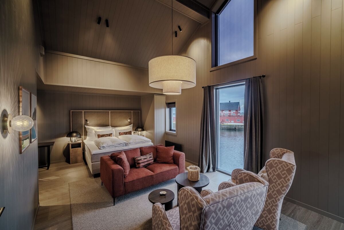 A modern hotel room with a large bed, a sofa, a small table, and a view of a body of water.