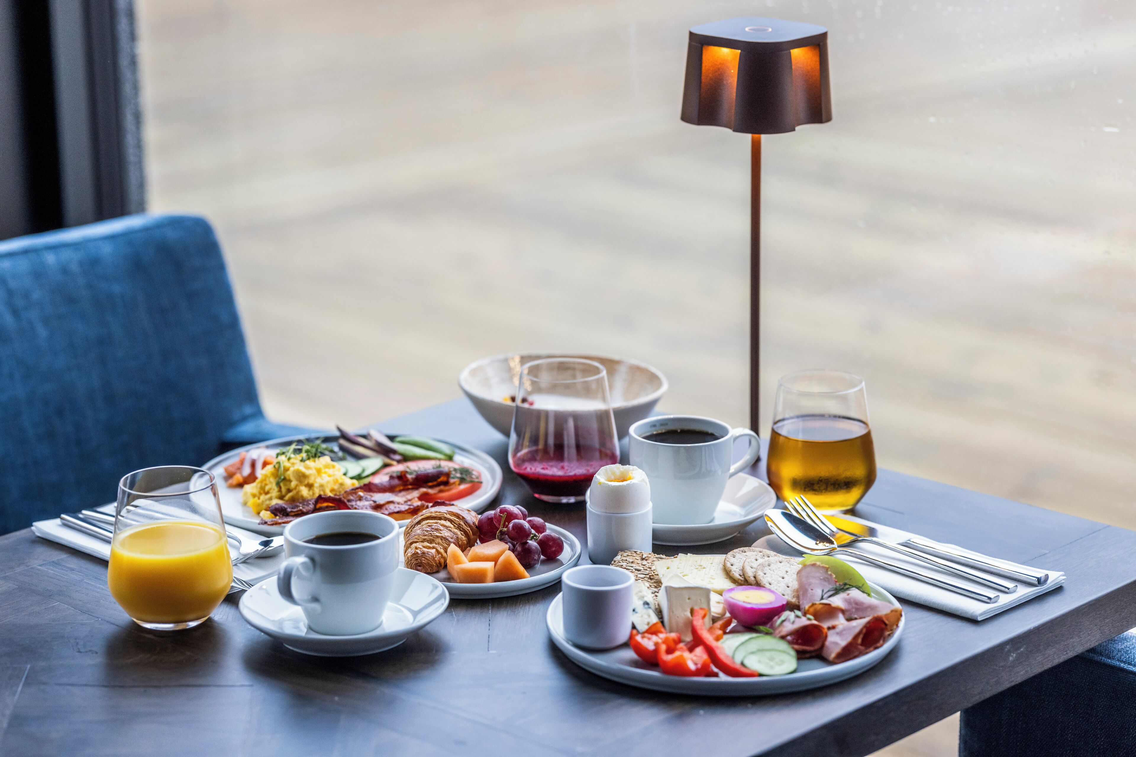 A breakfast table with plates of food, drinks, and a lamp.