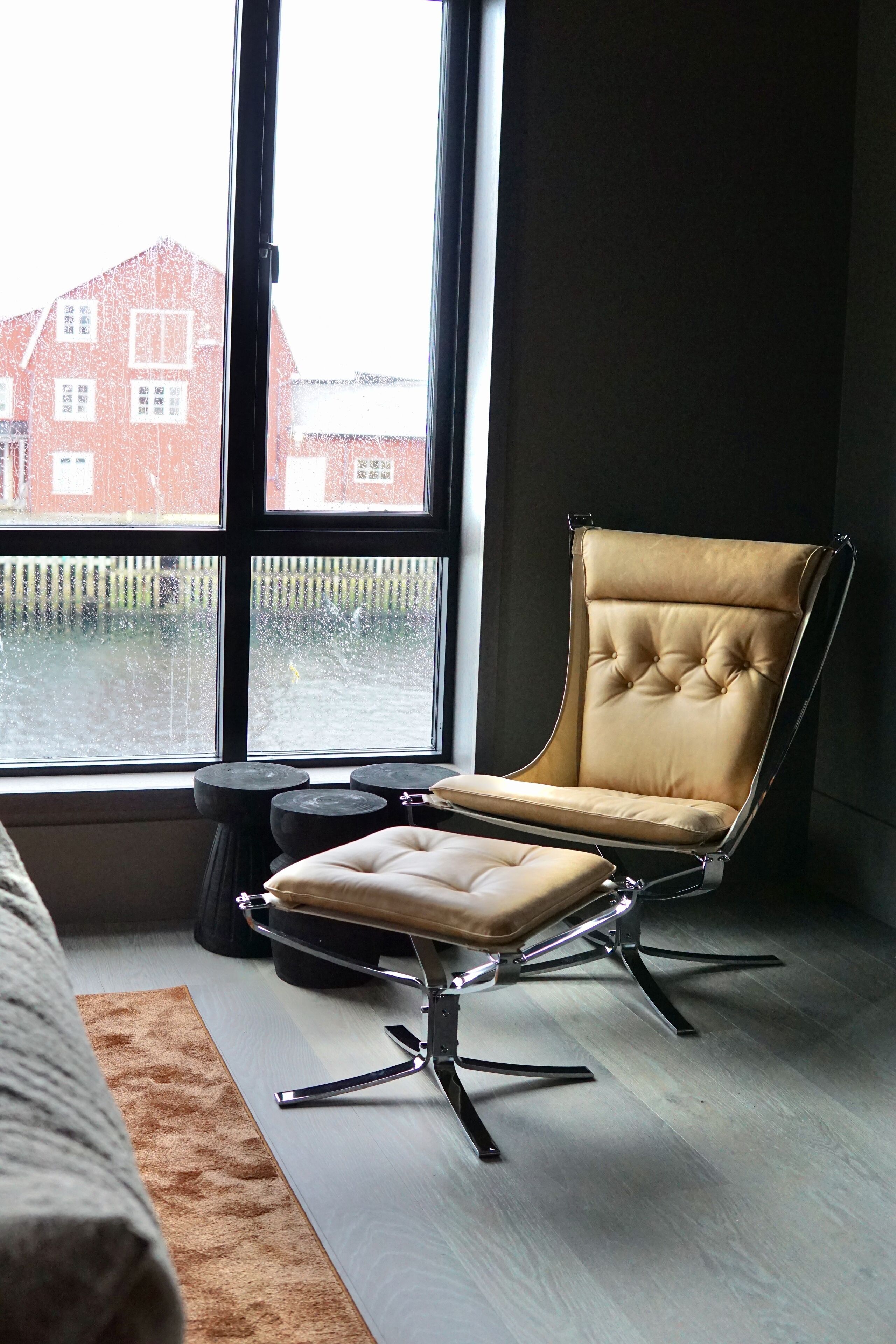 Une chambre moderne avec une grande fenêtre, un fauteuil en cuir capitonné, une petite table ronde et un tapis marron.