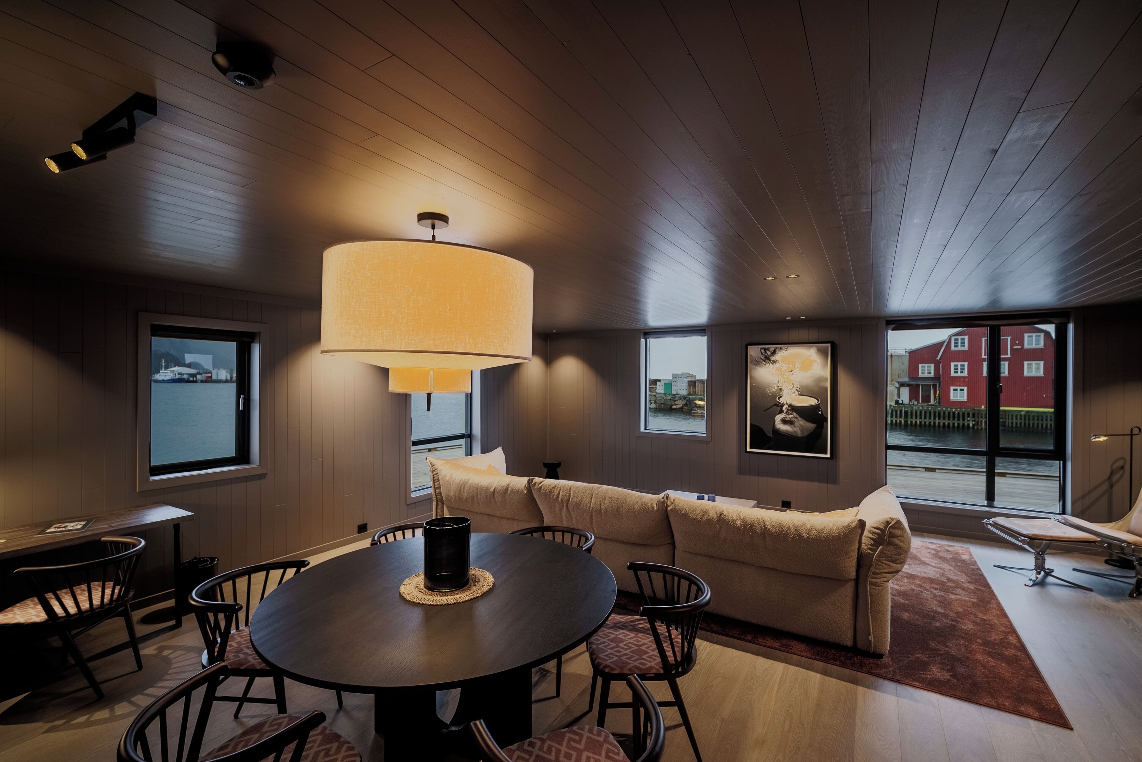 A modern dining area with a round table, chairs, a sofa, and a large floor lamp.