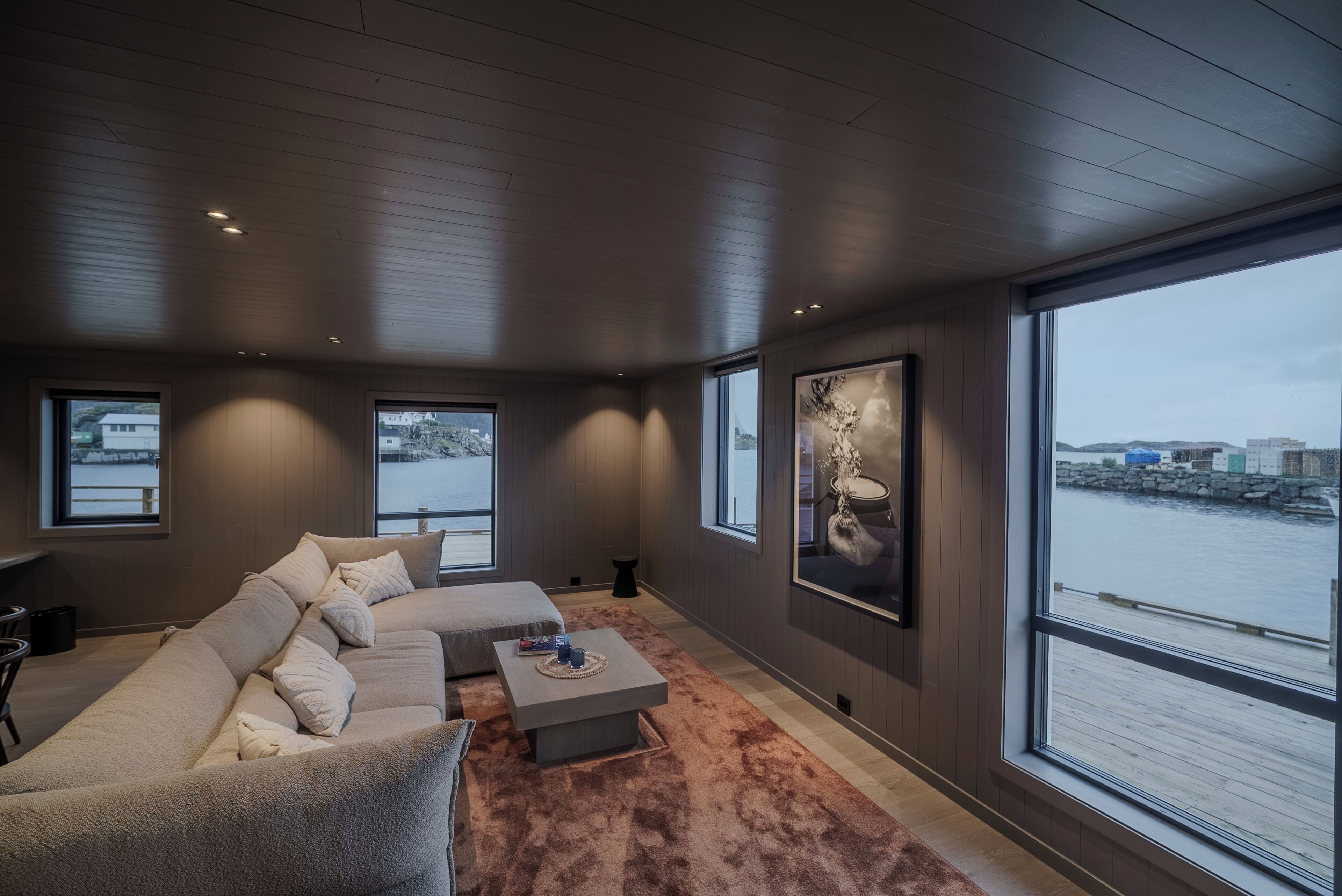 A modern living room with a large sofa, a coffee table, and a view of the water.
