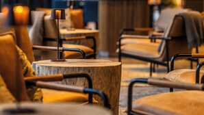 A modern cafe with wooden tables and cushioned chairs, a bar area in the background, and a person in the distance. - Henningsvær Bryggehotell - by Classic Norway Hotels (Vagan)